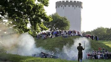 Una recreación histórica con una multitud observando, un cañón y una torre grande al fondo.