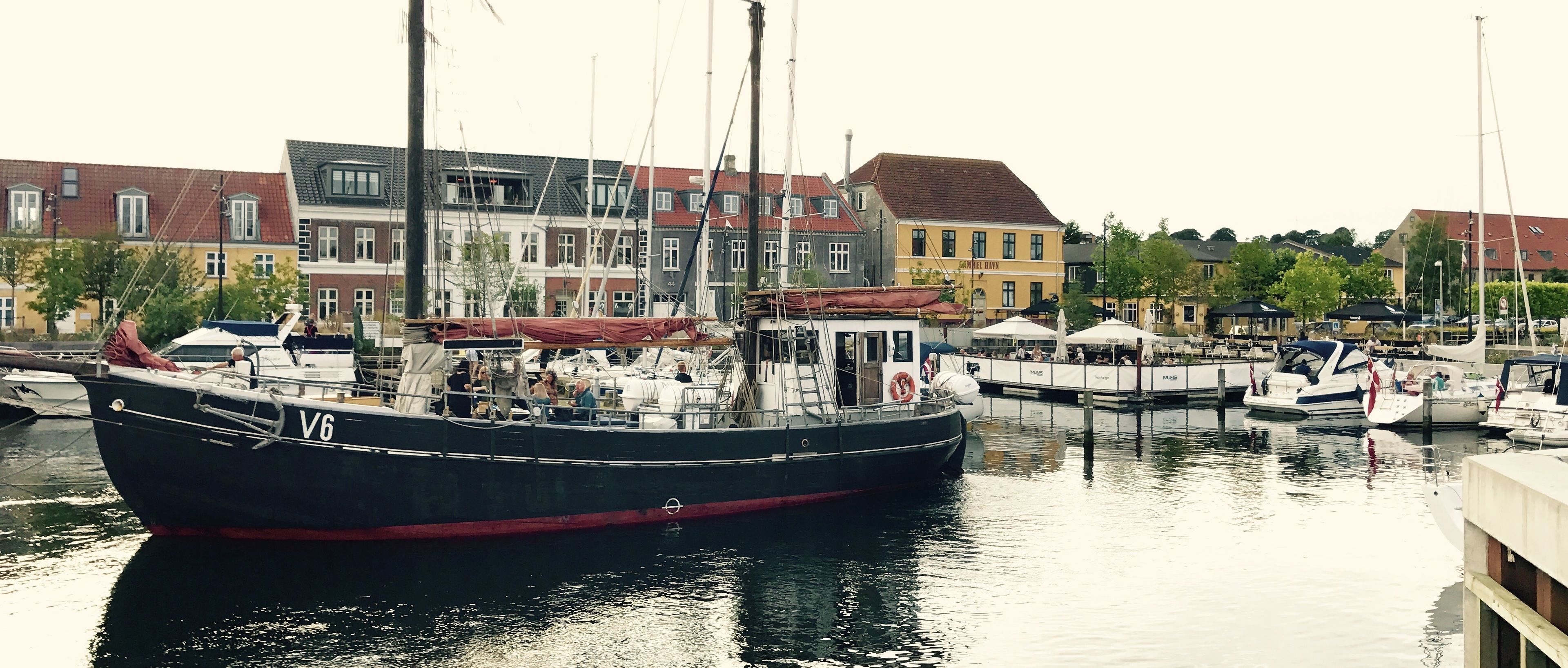 En småbåtshamn med flera båtar förtöjda, omgiven av höga byggnader med butiker och andra kommersiella verksamheter.