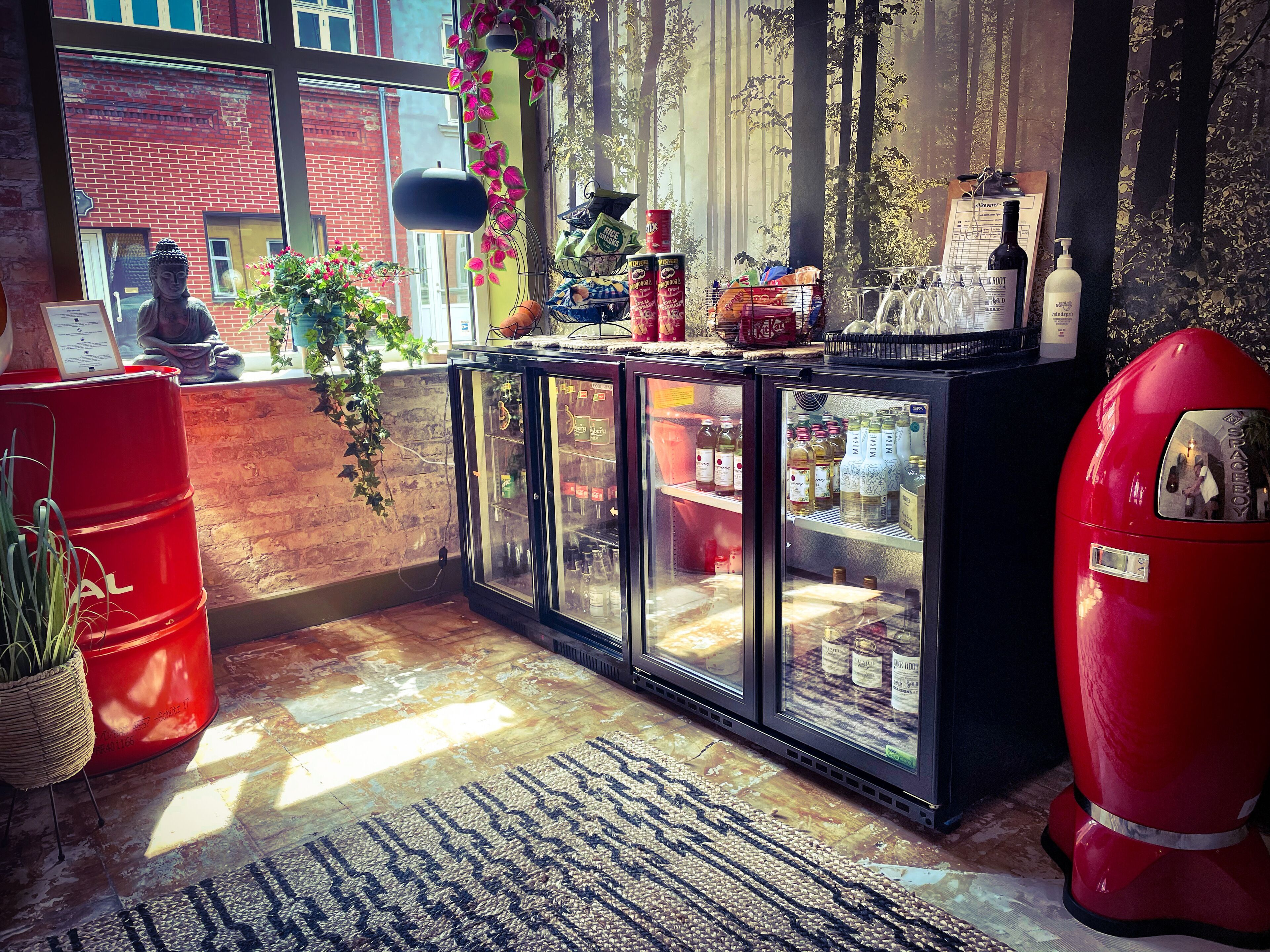 Una zona de bar con un barril rojo, un mueble de vidrio con botellas y una máquina expendedora roja.