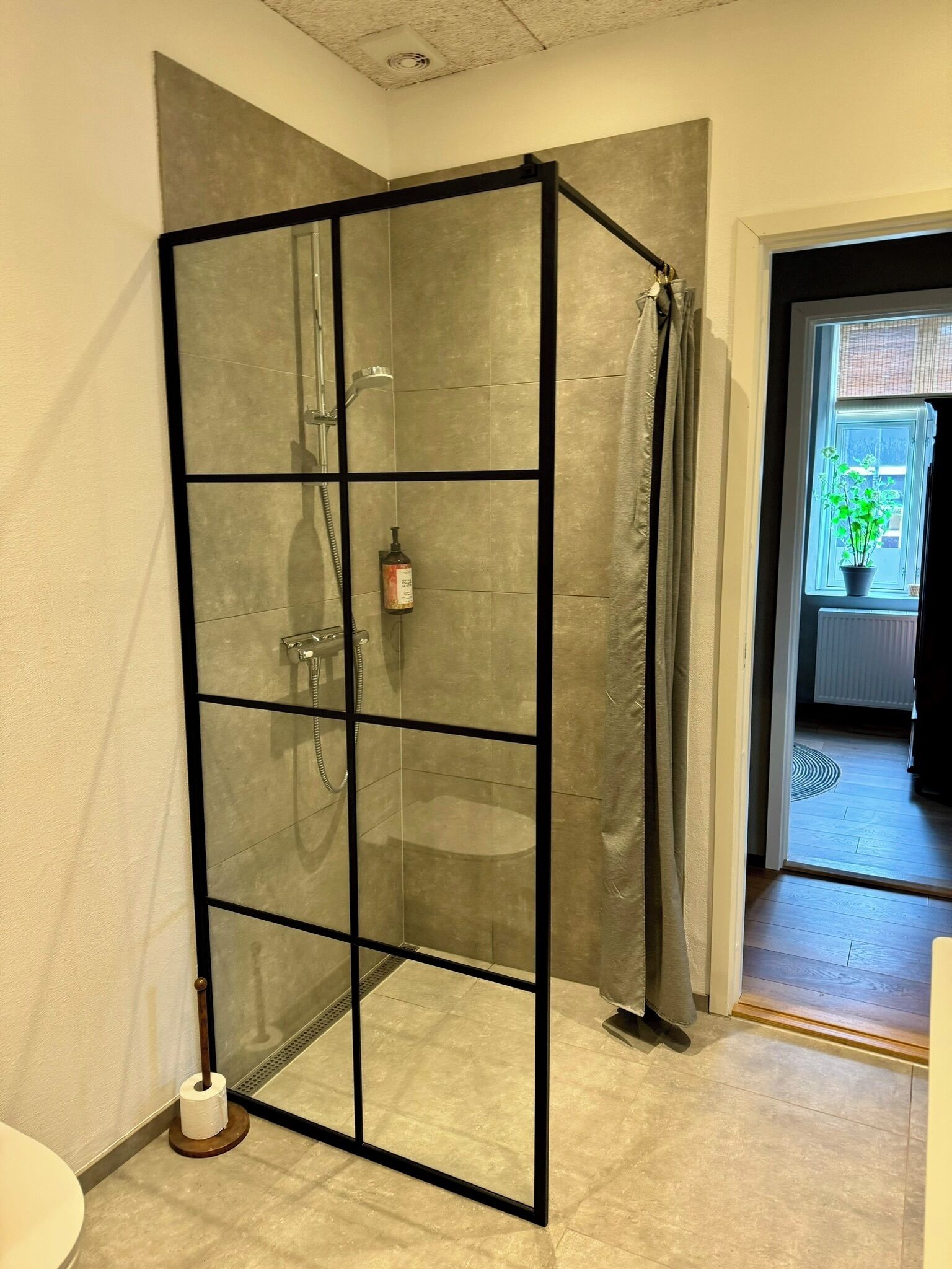 A glass-enclosed shower with a showerhead, a handheld showerhead, and a bottle of shampoo.