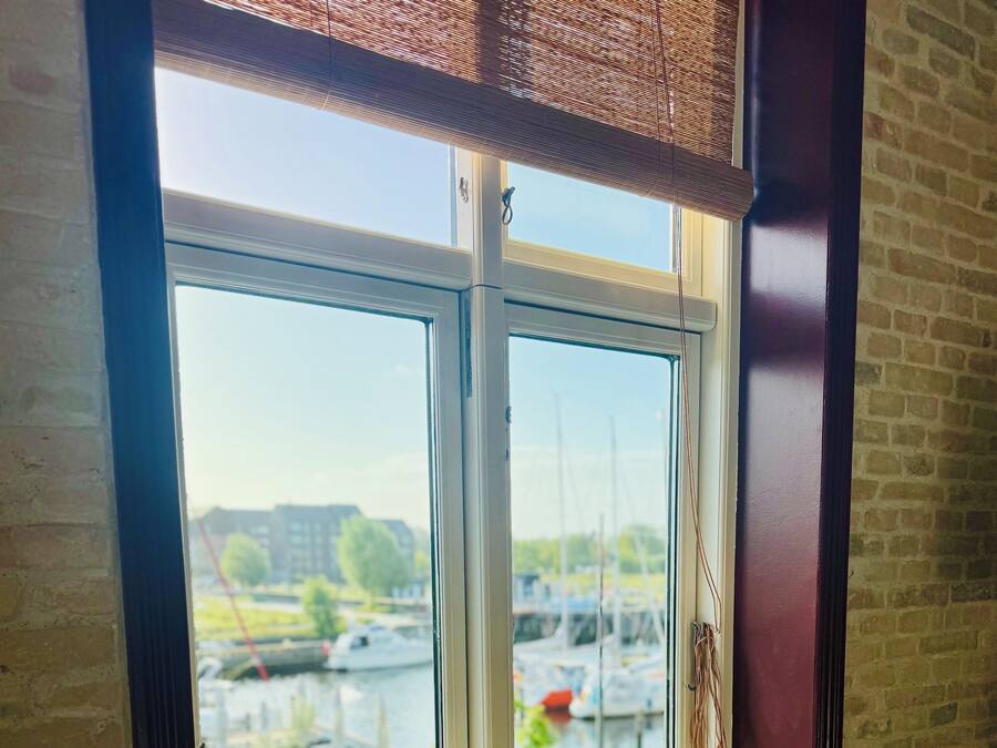 A room with a large window overlooking a marina, a radiator below the window, and a small table with a bottle and a decorative item.
