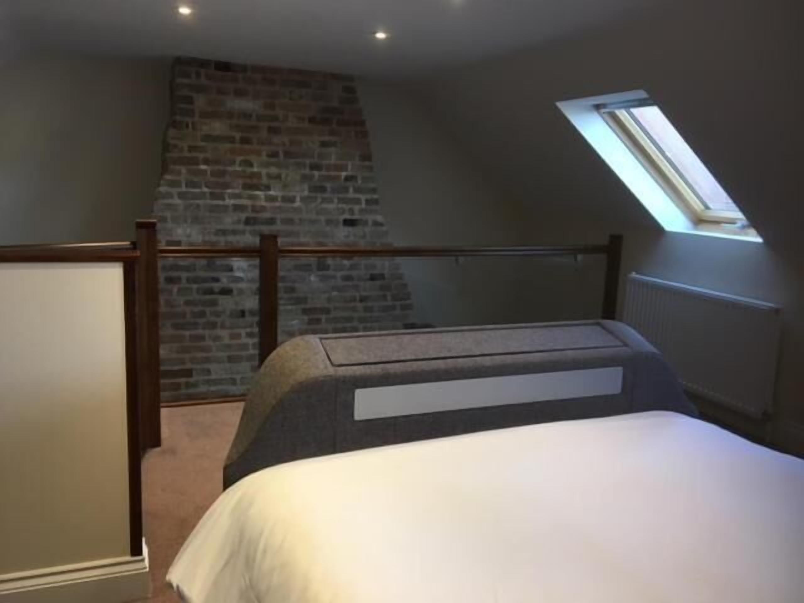 Un dormitorio con techo inclinado, pared de ladrillo, tragaluz y cama con cabecera.