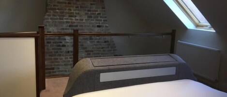 Un dormitorio con techo inclinado, pared de ladrillo, tragaluz y cama con cabecera.