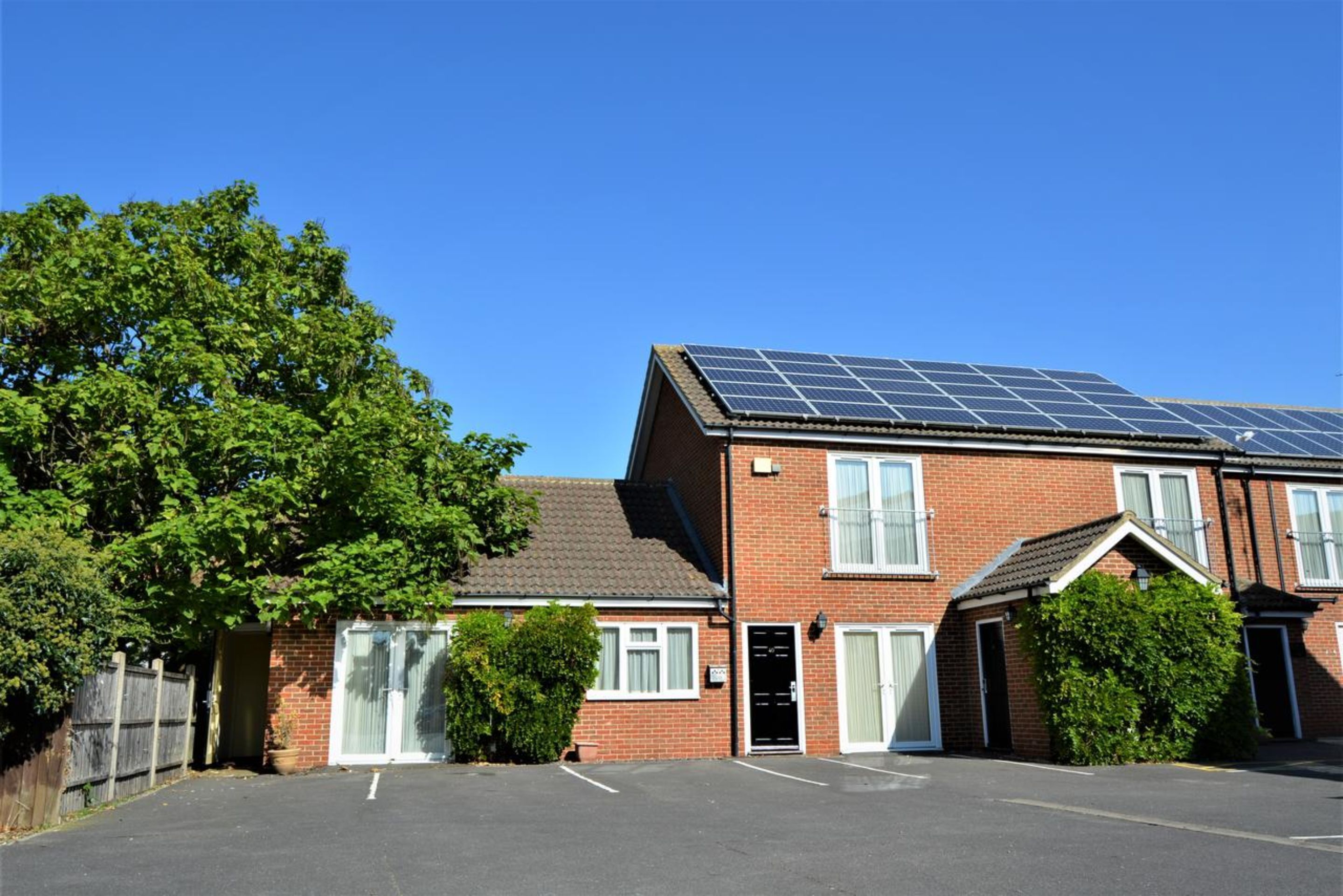 Une maison à deux étages, construite en briques, avec un toit équipé de panneaux solaires, un garage et une allée.