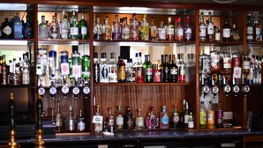 Un bar avec de nombreuses étagères remplies de bouteilles d’alcool et un comptoir où se trouvent une caisse enregistreuse et quelques bouteilles.