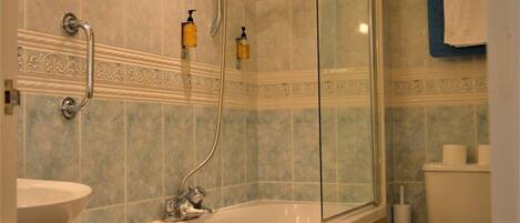 Un baño con bañera de madera, ducha con cerramiento de vidrio y un inodoro.