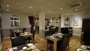 Une salle à manger d’hôtel avec plusieurs tables et chaises, une horloge au mur et un tableau encadré.