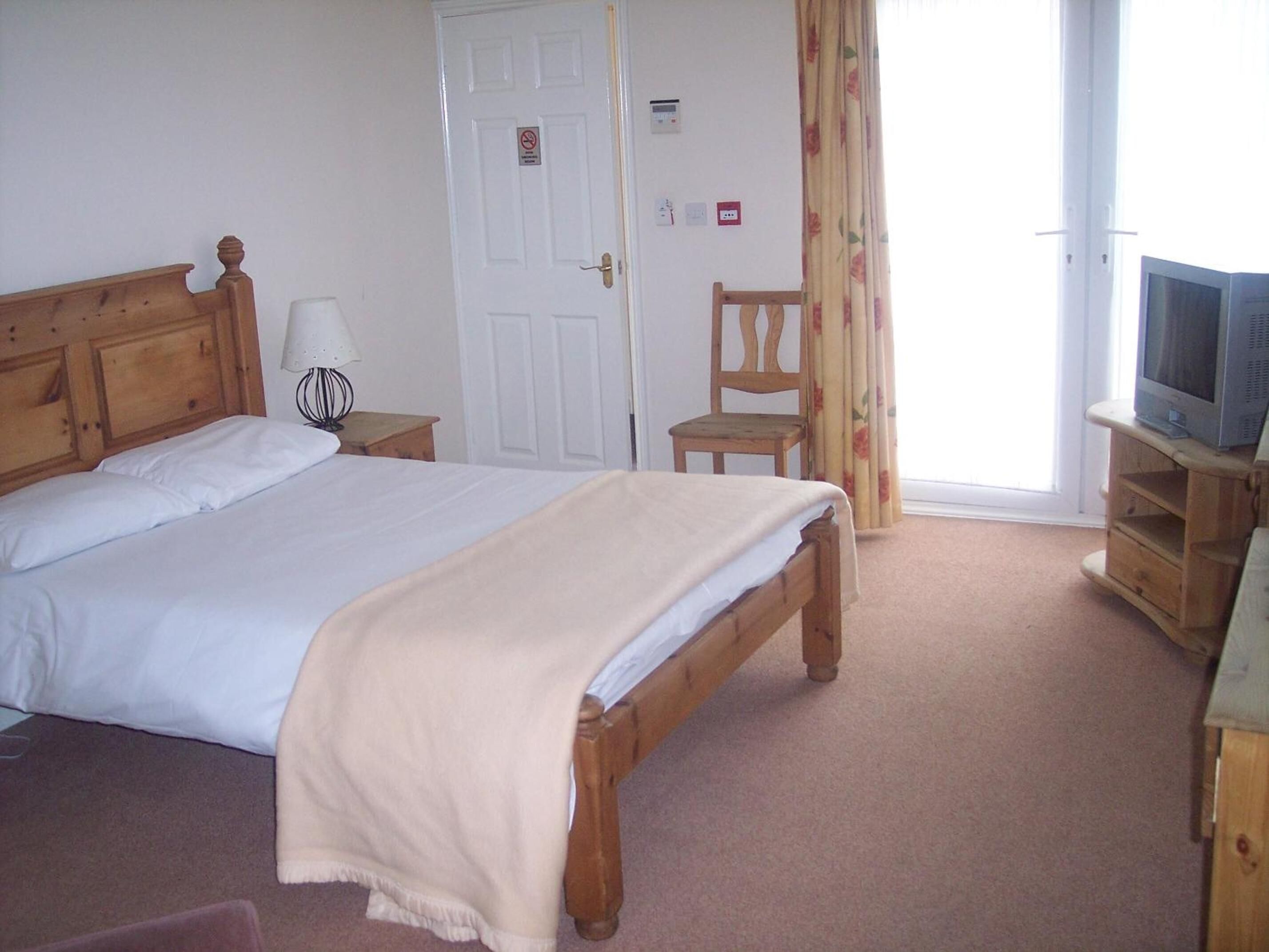 A bedroom with a wooden bed, a chair, a television on a wooden stand, and a door with a sign.