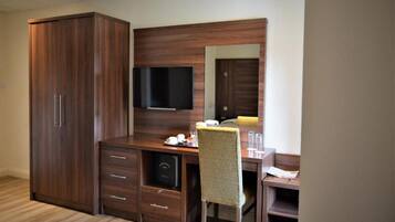 Quarto de hotel com guarda-roupa de madeira, uma escrivaninha com cadeira, televisão de tela plana e um espelho.