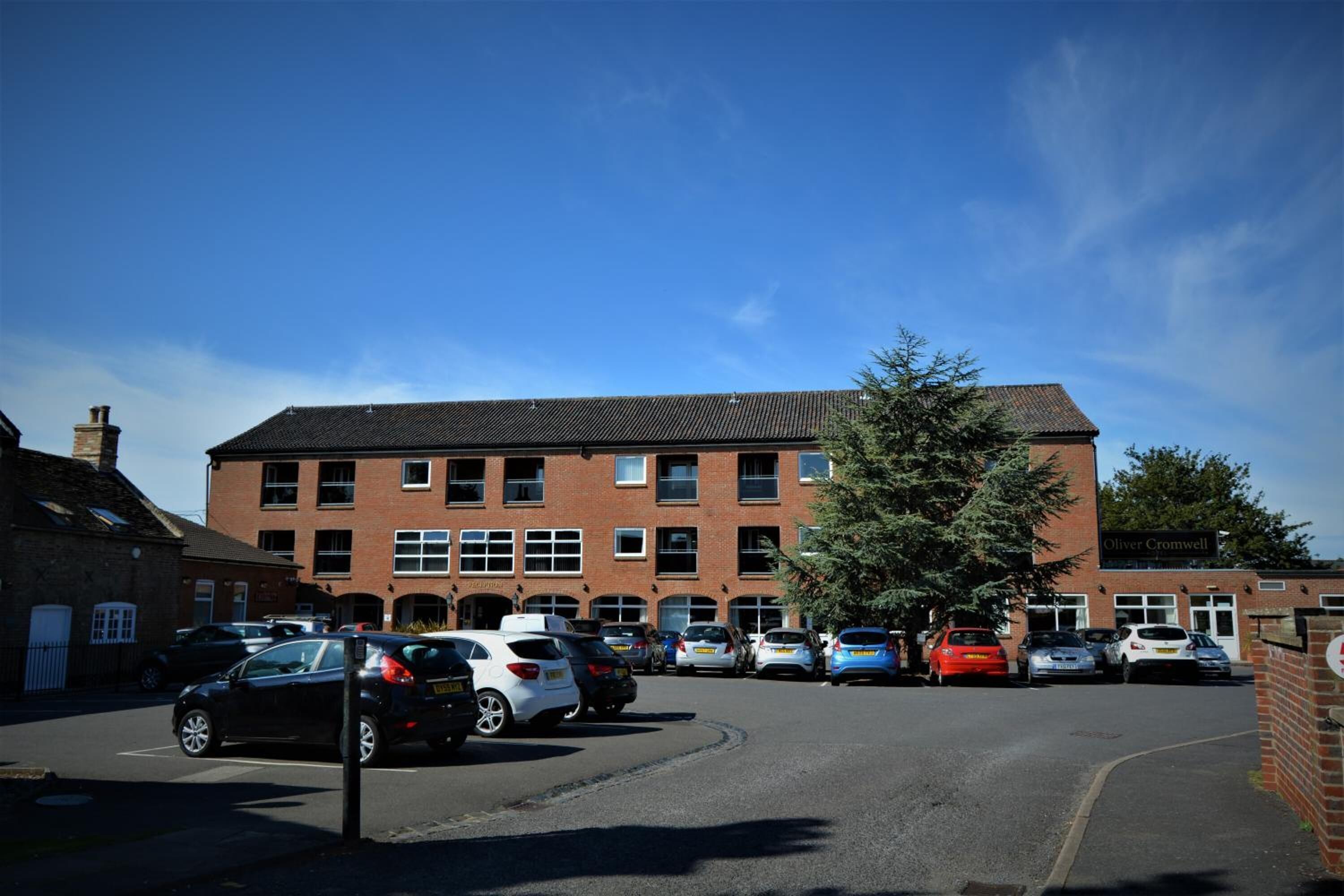 A parking lot with several cars and a building with multiple windows and a sign that reads "Oliver Cromwell".