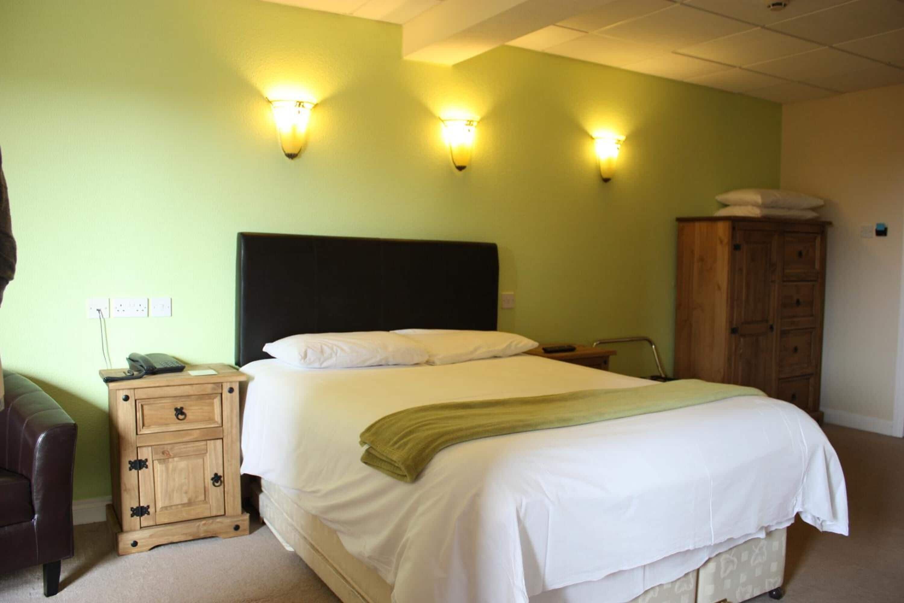 Una habitación de hotel con cama, mesita de noche, lámpara, armario e iluminación en la pared.
