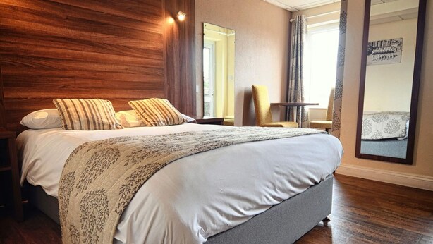 Une chambre d’hôtel moderne avec un grand lit, une tête de lit en bois et une vue sur la ville.
