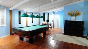 Een pooltafel in een ruimte met blauwe wanden, een houten vloer en een piano.