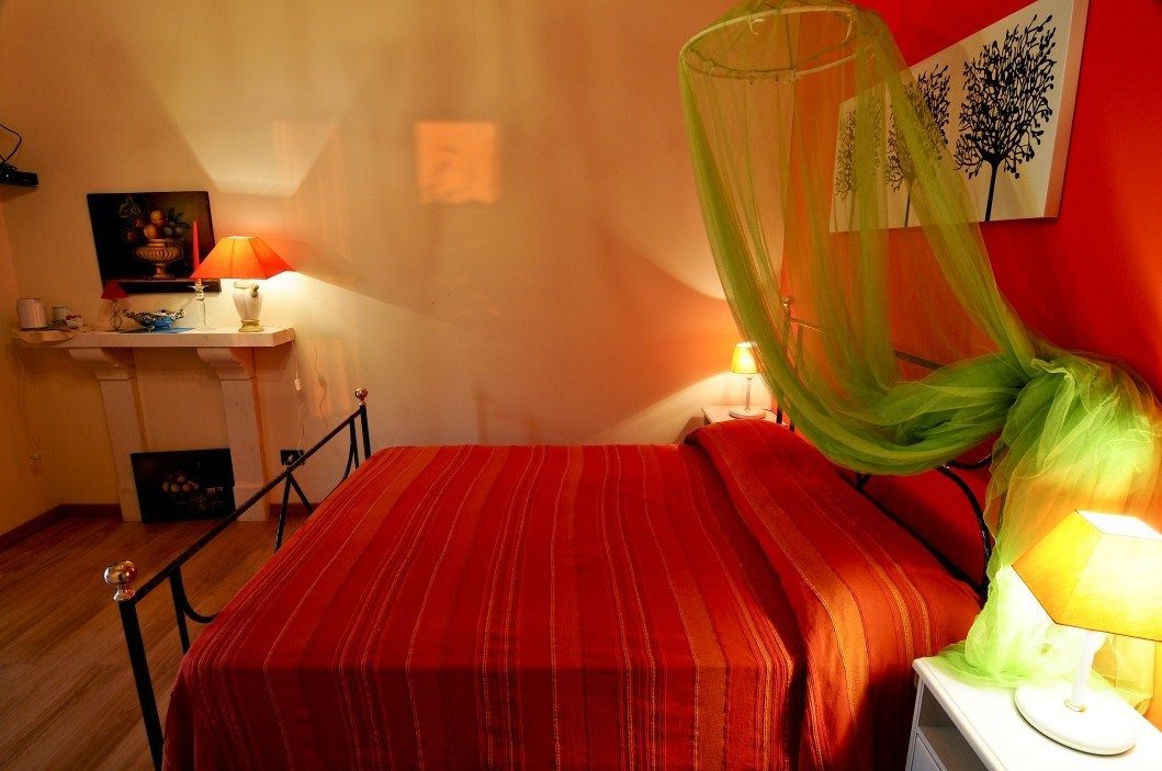 Ein Zimmer mit einem Bett, einem Nachttisch mit Lampe, einem Wandbild und einem Fenster mit durchsichtigem Vorhang.