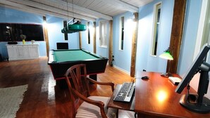 Een kamer met een pooltafel, een bureau met een computer en een stoel.