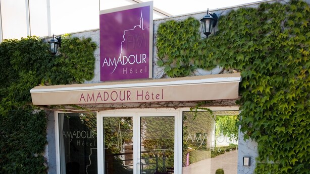 An outdoor seating area with tables and chairs, surrounded by planters with shrubs. - Amadour Hôtel (Rocamadour)