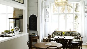 A dining area with a round table, chairs, a chandelier, a chalkboard, and a window with curtains. - Hotel Mundal (Sogndal)