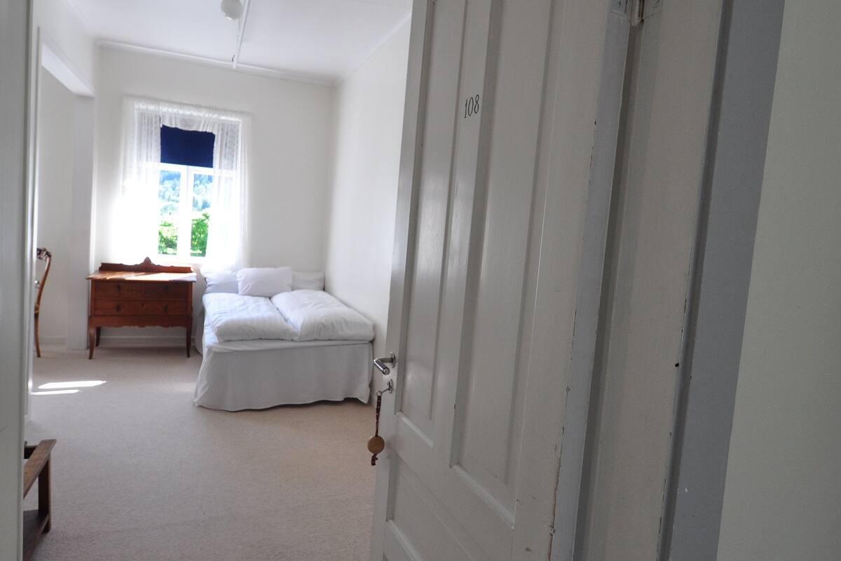 A bedroom with a bed, a dresser, and a window with curtains.