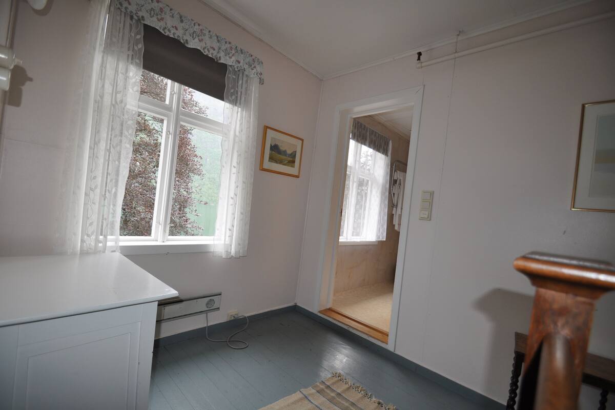 A room with a window, a door, a radiator, and a wooden chair.