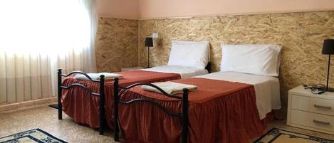 Una habitación con dos camas, una mesita de noche, una lámpara y un ventanal con cortinas.
