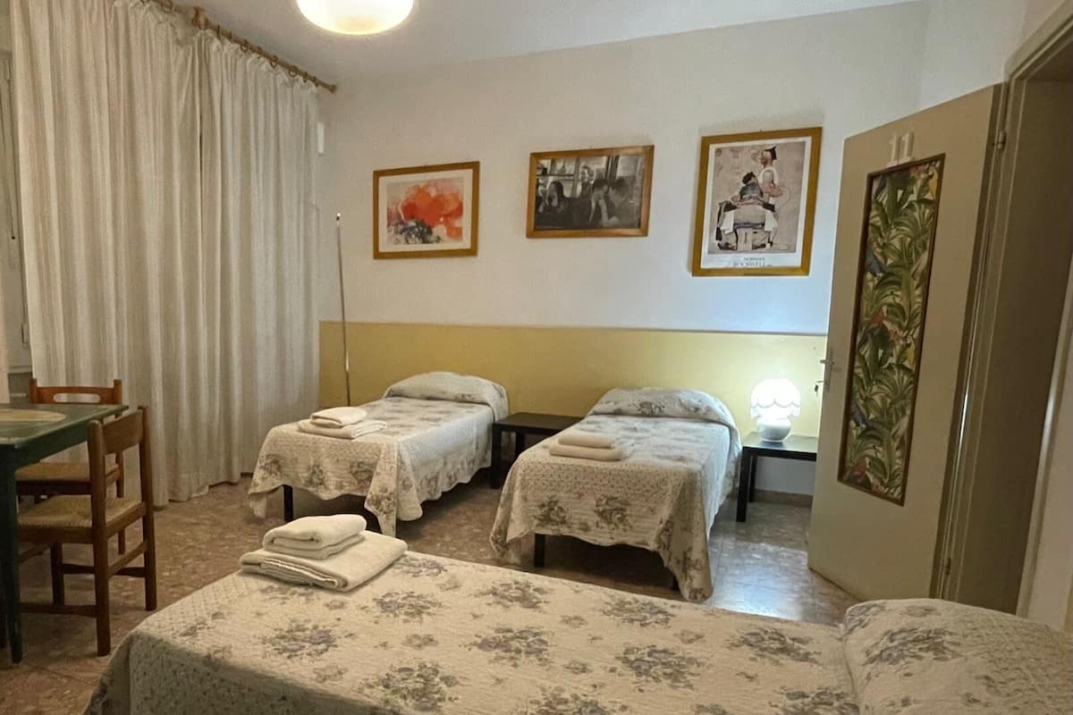 Une chambre d’hôtel avec deux lits simples, une petite table avec une chaise, une lampe et trois tableaux encadrés accrochés au mur.