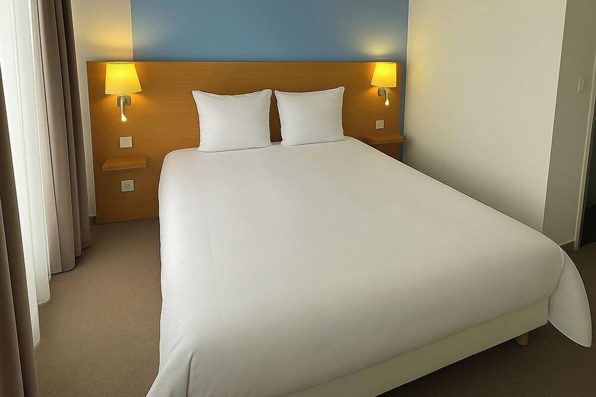 A hotel room with a large bed, two bedside lamps, a night light, and a wall-mounted light fixture.