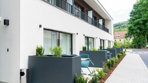 Un bâtiment moderne avec une façade blanche, de grandes fenêtres et un balcon agrémenté de chaises bleues.