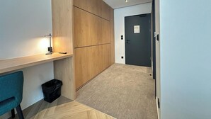 Un couloir moderne et minimaliste, agrémenté d’une cloison en bois, d’un bureau avec une lampe et d’une porte sur laquelle est apposée une plaque.