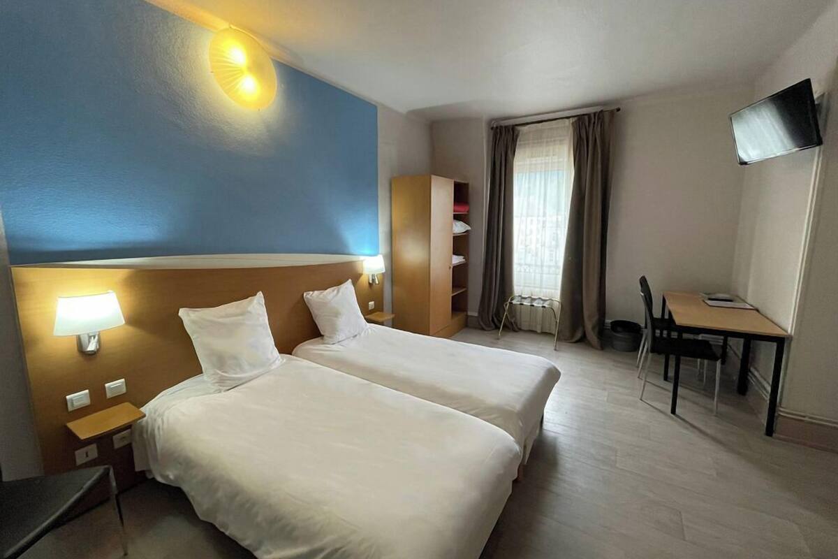 A hotel room with two beds, a desk, a chair, a TV, and a window with curtains.