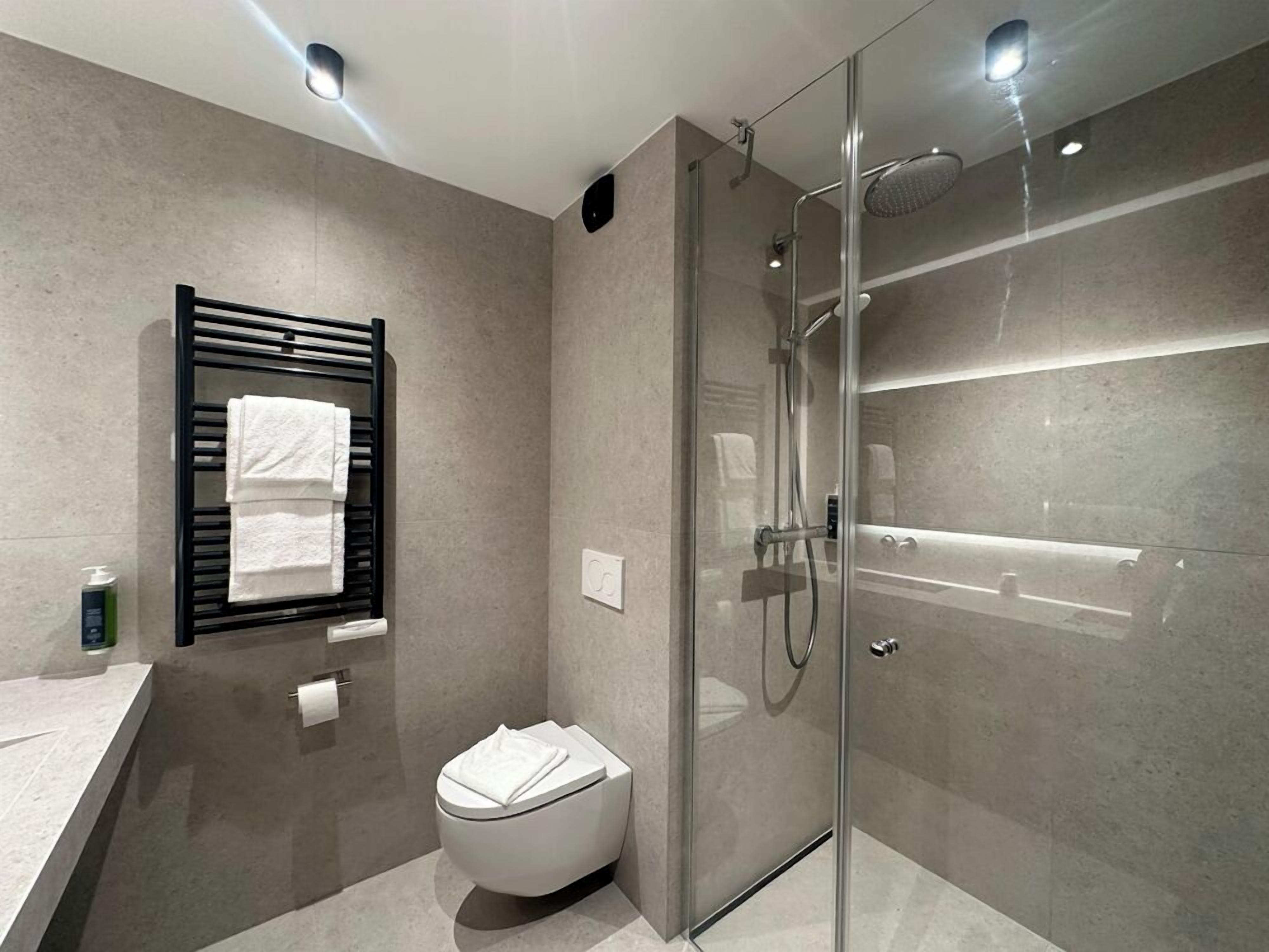 Un baño moderno con ducha de vidrio, inodoro, toallero y lavamanos.