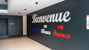 Un couloir dont un mur est orné de l’inscription « Bienvenue en Alsace, en France », déclinée en plusieurs langues.