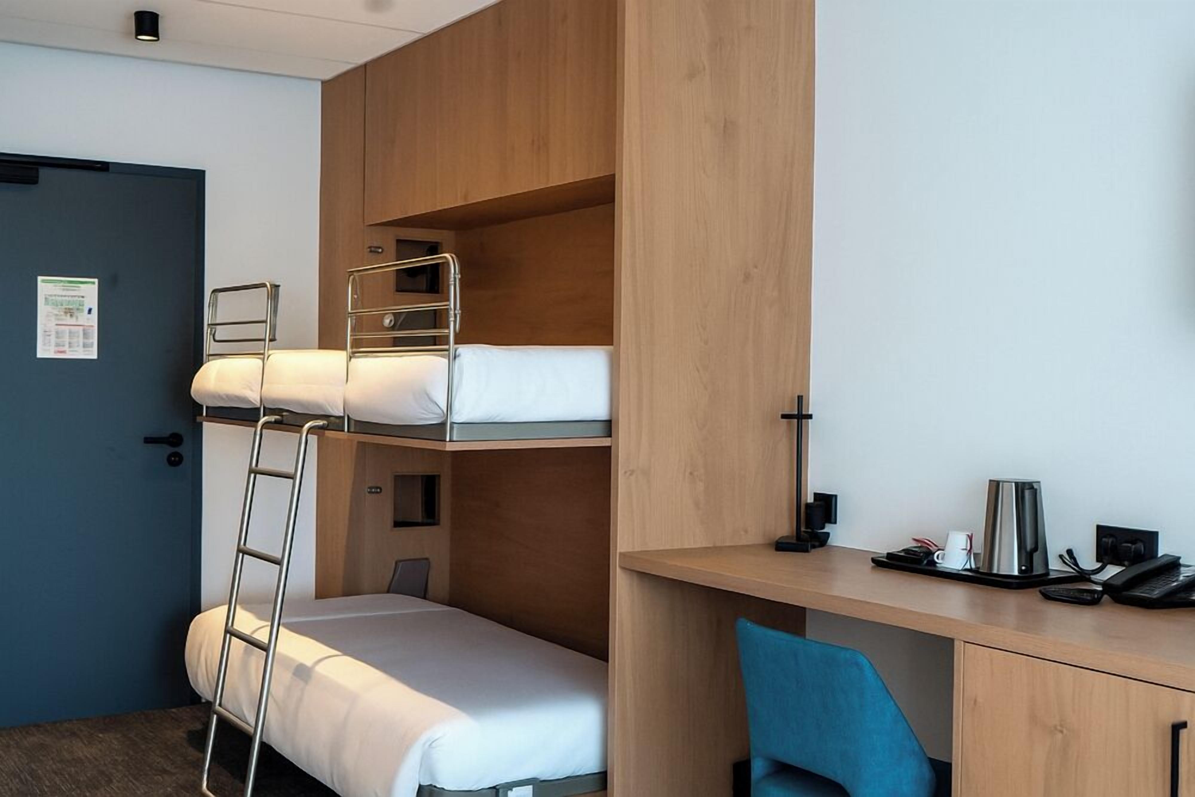 Una cama litera con escalera, un escritorio con silla y una cafetera.