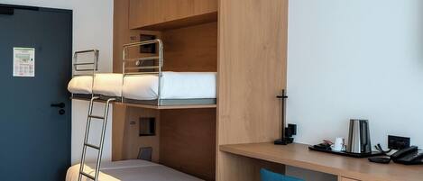 Una cama litera con escalera, un escritorio con silla y una cafetera.
