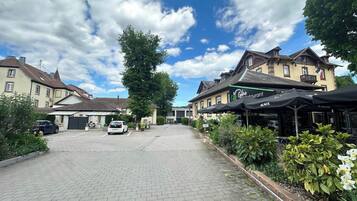 A paved street with buildings, a parked car, and outdoor seating at a restaurant.