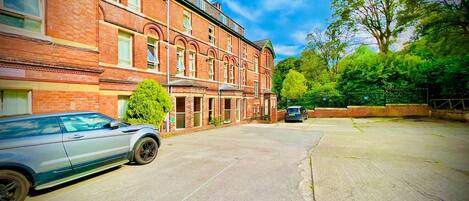 A building with a brick facade, a car parked in front, and a tree to the right.