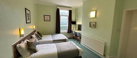 A hotel room with two beds, a desk, a chair, a window with curtains, and a radiator.