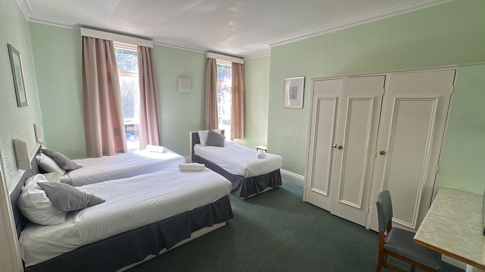 A hotel room with two beds, a desk, and a wardrobe.