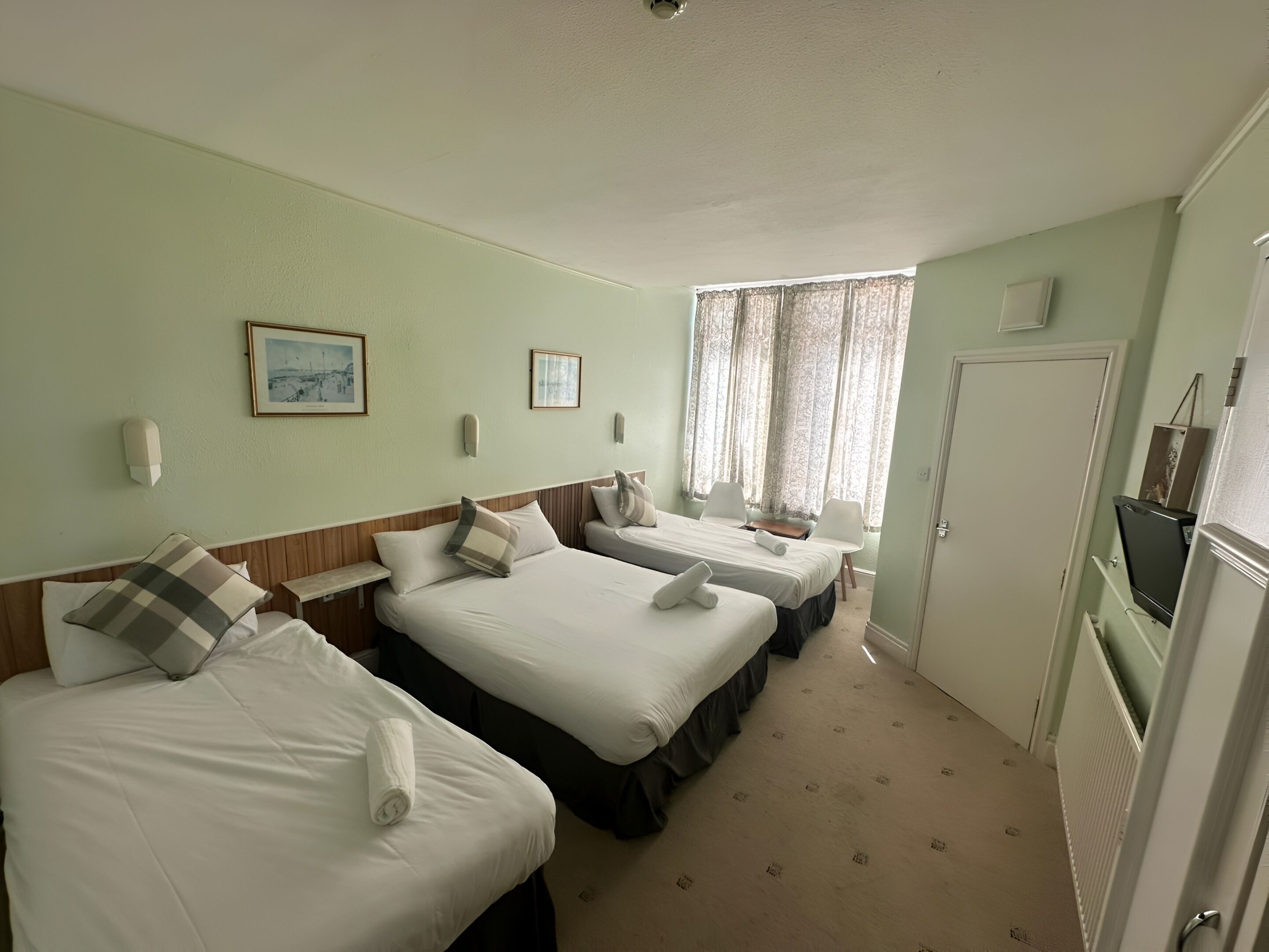 A hotel room with two beds, a desk, a television, and a window with curtains.
