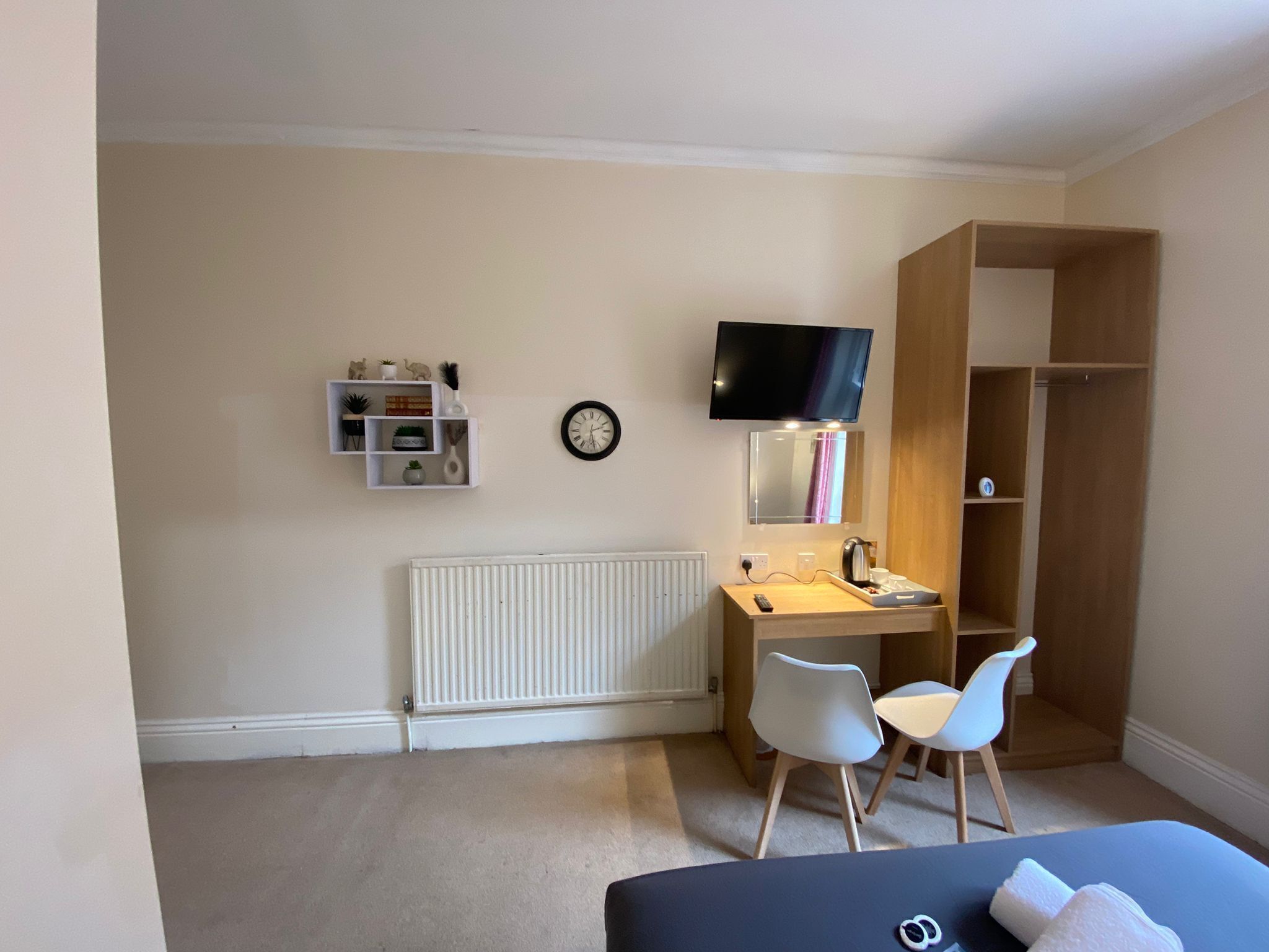 Une chambre à coucher comprenant un lit, un bureau, deux chaises, un téléviseur, un radiateur et une armoire.