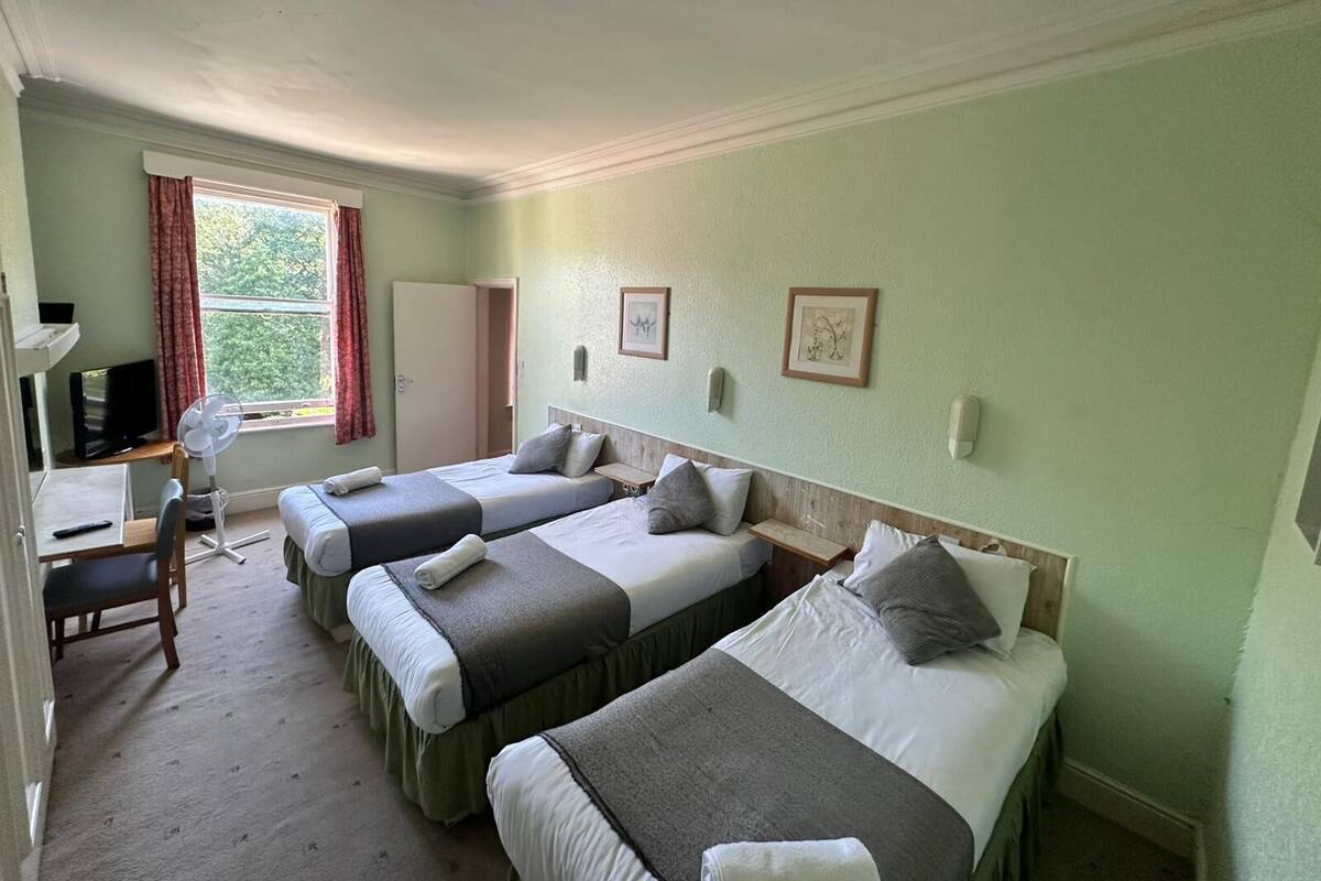 A hotel room with two single beds, a desk with a chair, a TV, and a window with curtains.