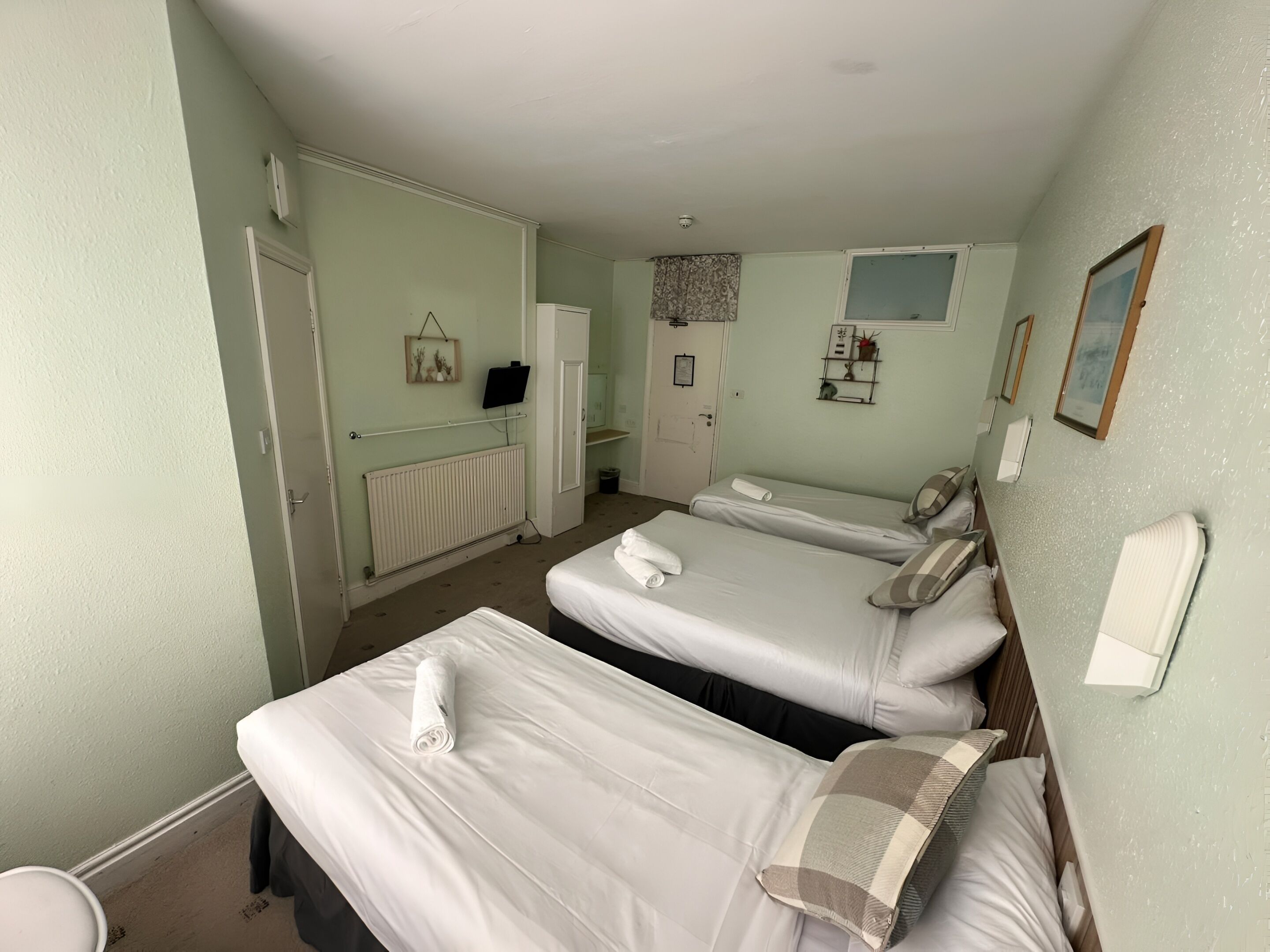 A hotel room with two beds, a radiator, a small desk, a television, and a bathroom.