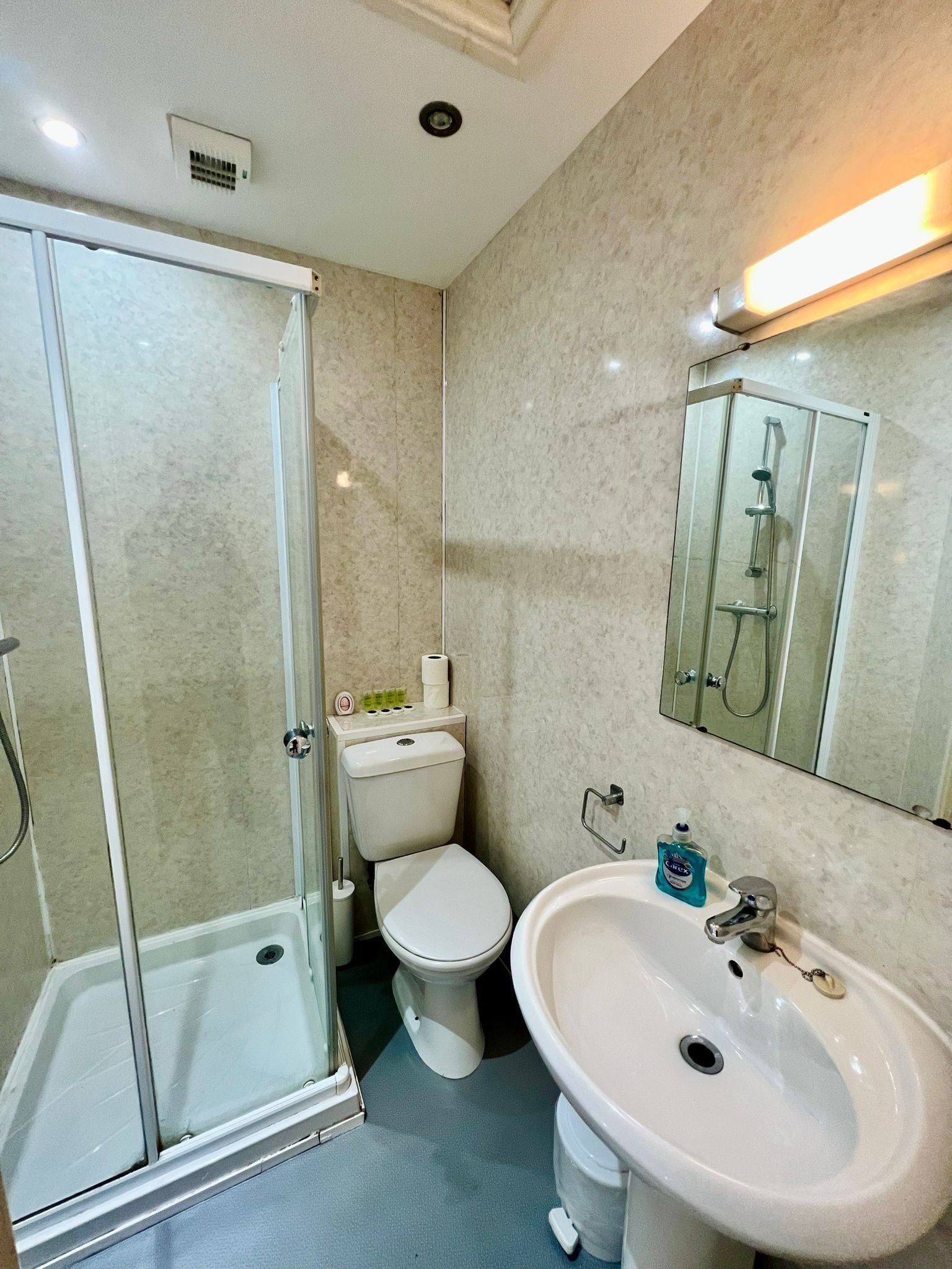 Egy fürdőszoba, amelyben üvegfalas zuhanyzó, WC, mosdókagyló és tükör található.