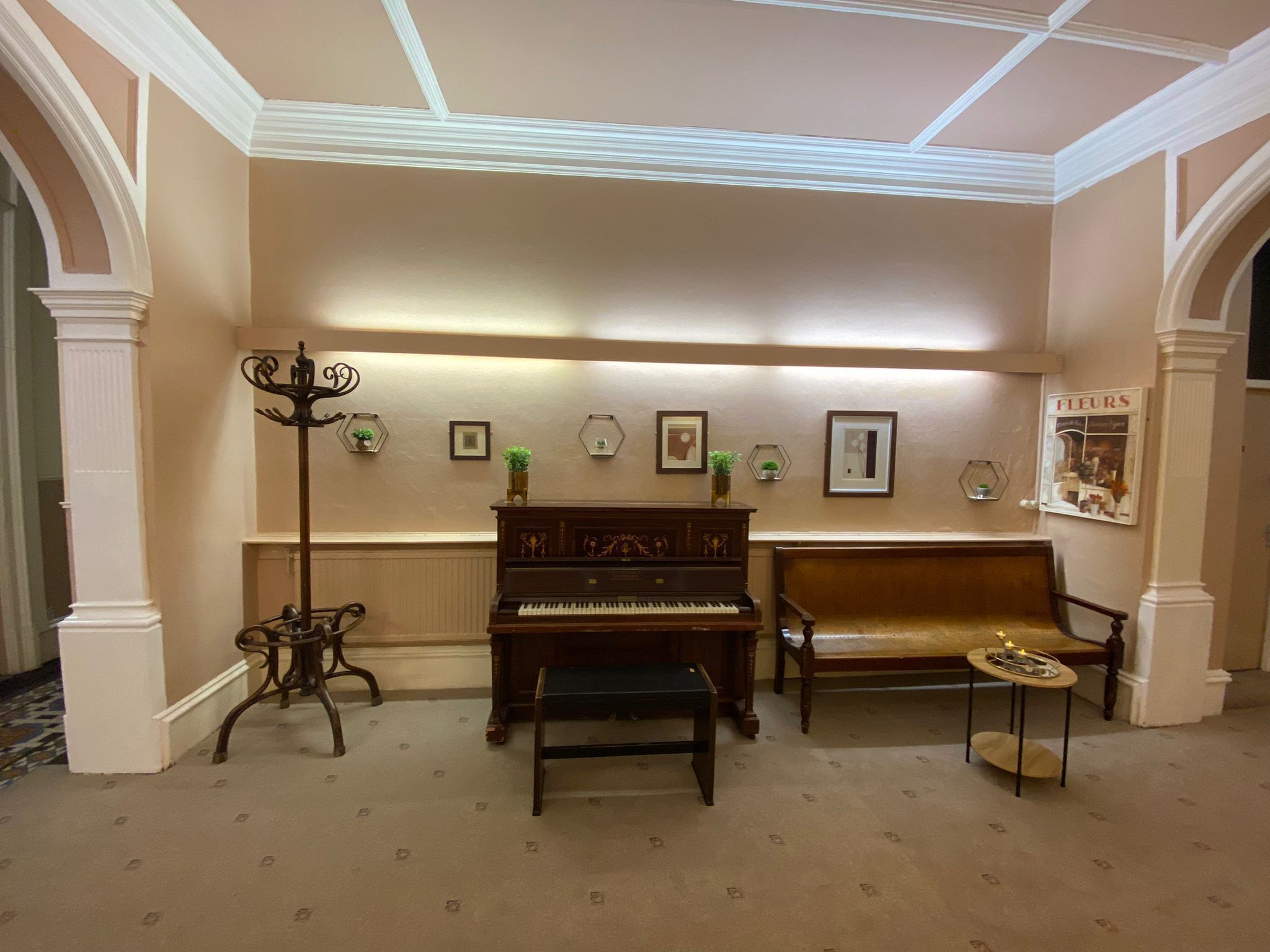 Una habitación con un piano, un banco, una lámpara de pie y una pared decorada con cuadros.