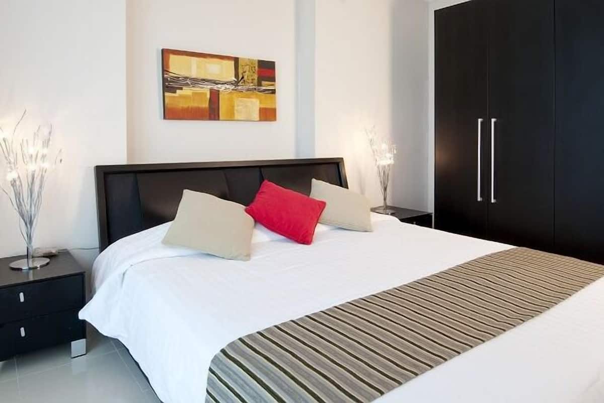 A modern bedroom with a large bed, a black wardrobe, and a painting on the wall.
