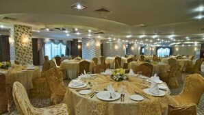 A banquet hall with round tables covered in white tablecloths, gold chairs, and floral centerpieces. - Retaj Residence Al Corniche (Doha)