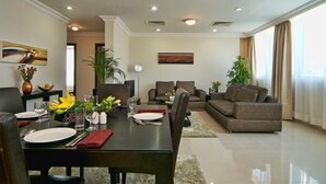 A modern living room with a dining area, featuring a sofa set, a dining table set for two, and a large window with curtains. - Retaj Residence Al Corniche (Doha)