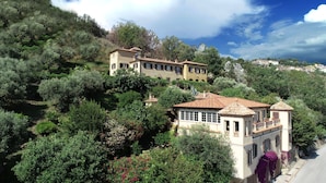 Une villa située sur une colline, composée de plusieurs bâtiments, et entourée d’une végétation luxuriante et d’arbres.