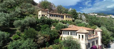 A hillside villa with multiple buildings, surrounded by lush greenery and trees.