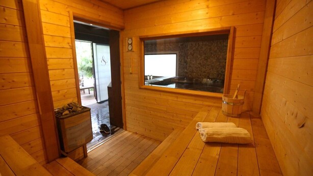 Een houten sauna met een bank, een raam en een handdoek.