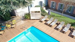 Een houten terras met een zwembad, ligstoelen en een overdekte zithoek.